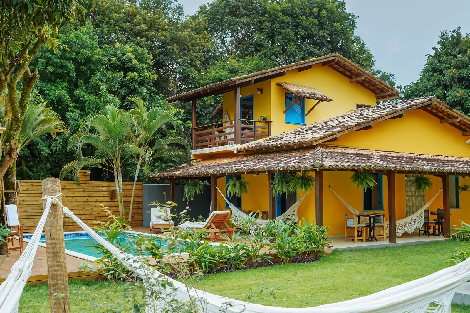 Fachada amarela da pousada com o jardim e a piscina