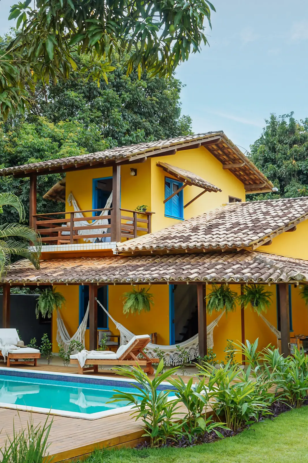 Casa amarela com varandas de madeira e a piscina em primeiro plano