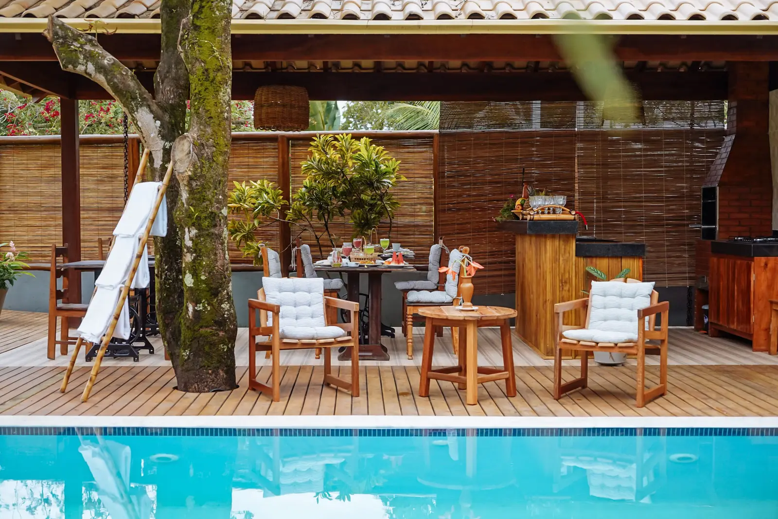 Deck com mesas à sombra das árvores junto à piscina