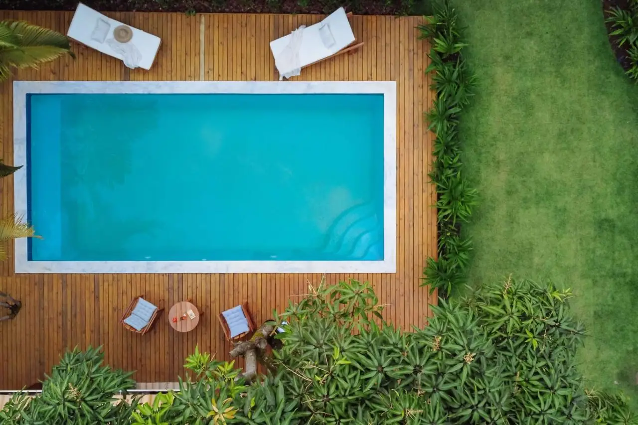 Vista aérea da piscina com deck de madeira cercada pelo jardim tropical