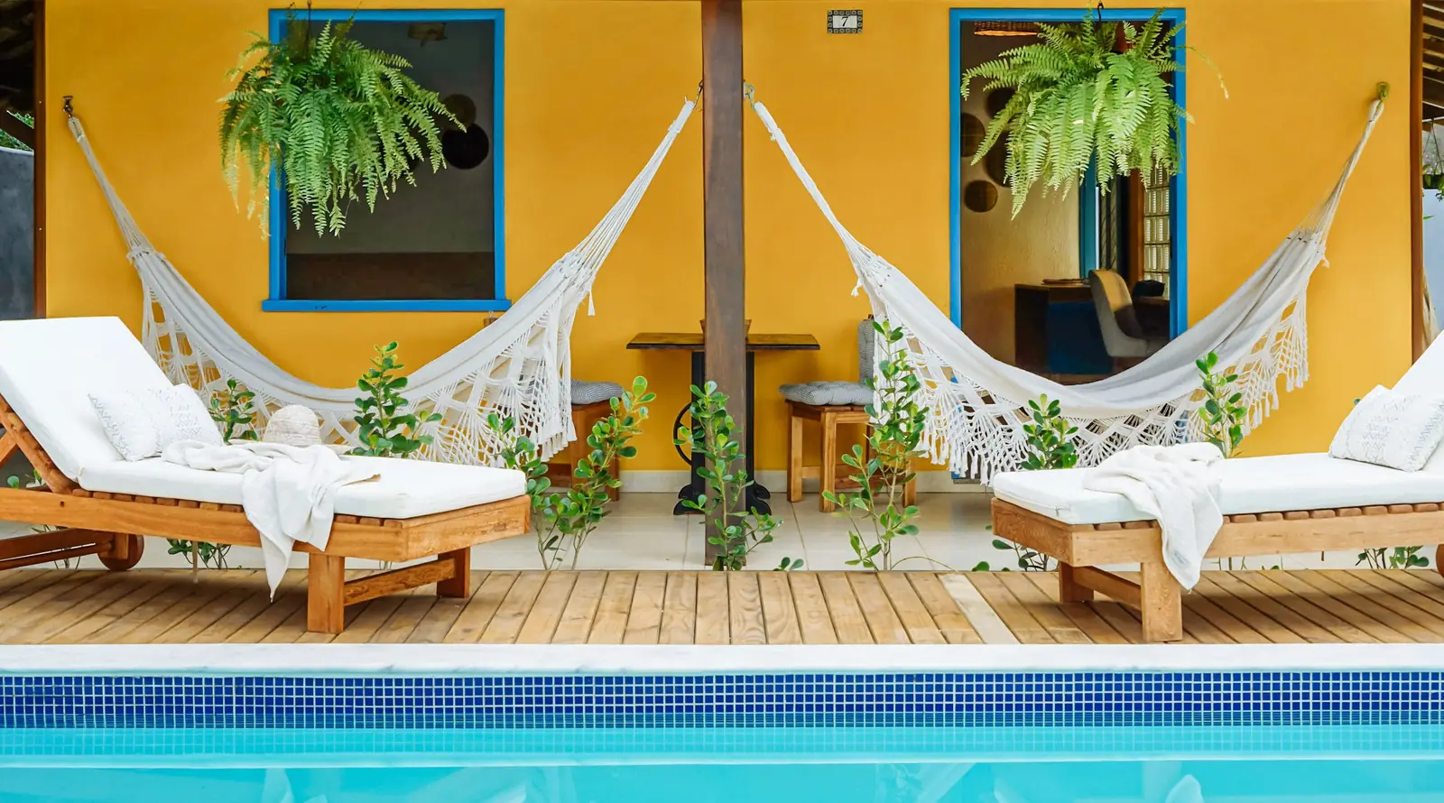 Redes e espreguiçadeiras na fachada amarela à beira da piscina